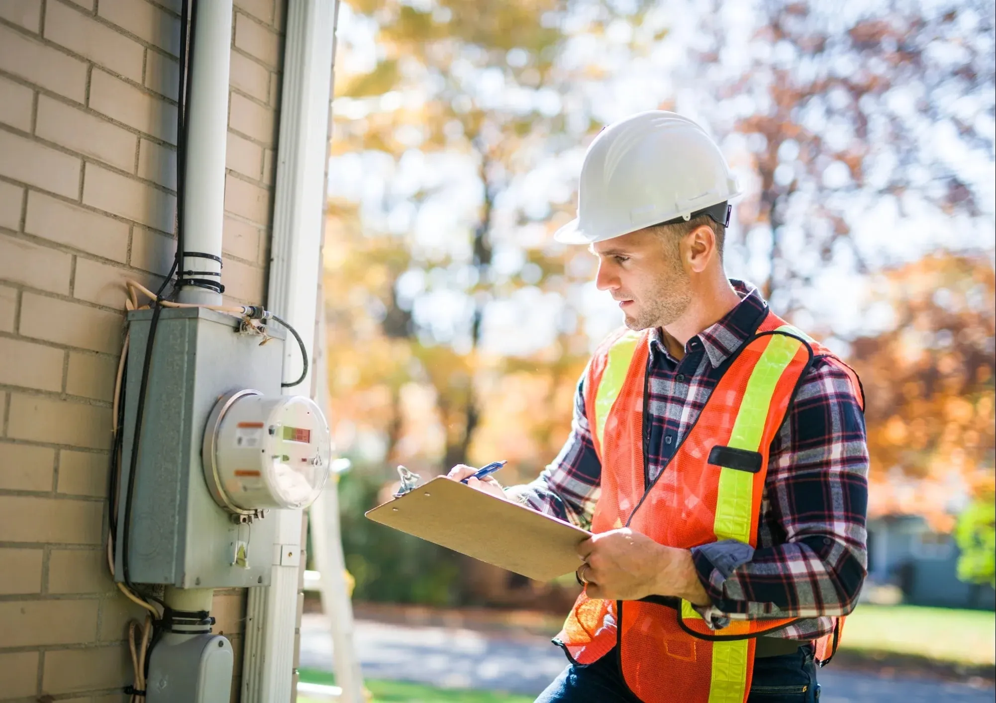 Electrician with a clipboard checking an outdoor electric meter on the side of a house