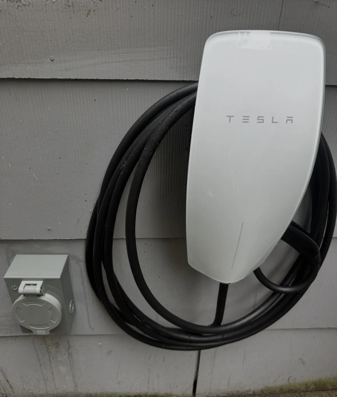 A Tesla Wall Connector EV charger mounted on the exterior siding of a home