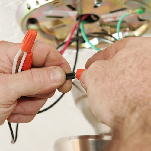 A closeup of an electrician's hands as he connects wires using a wire-nut.  All work is being performed to code by a licensed master electrician.